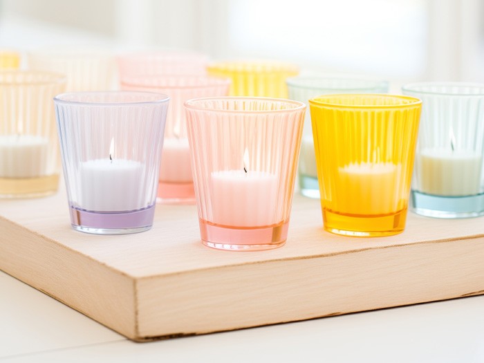 Bougies votives allumées dans des pots transparents de couleur pastel.